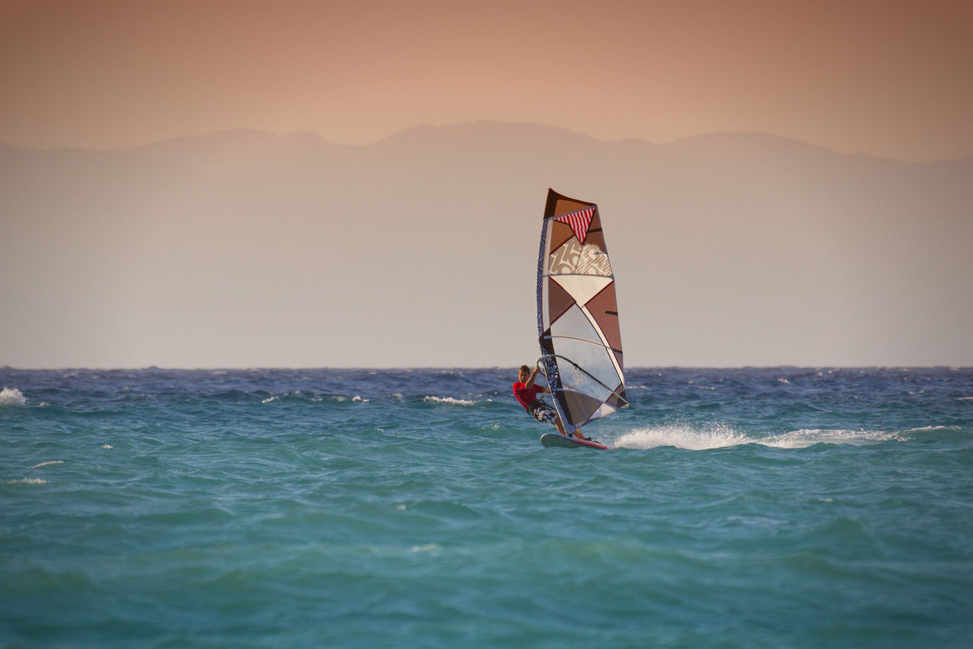 Windsurfing in Rhodes Greece_Man surfing on blue with oceanwith red sky