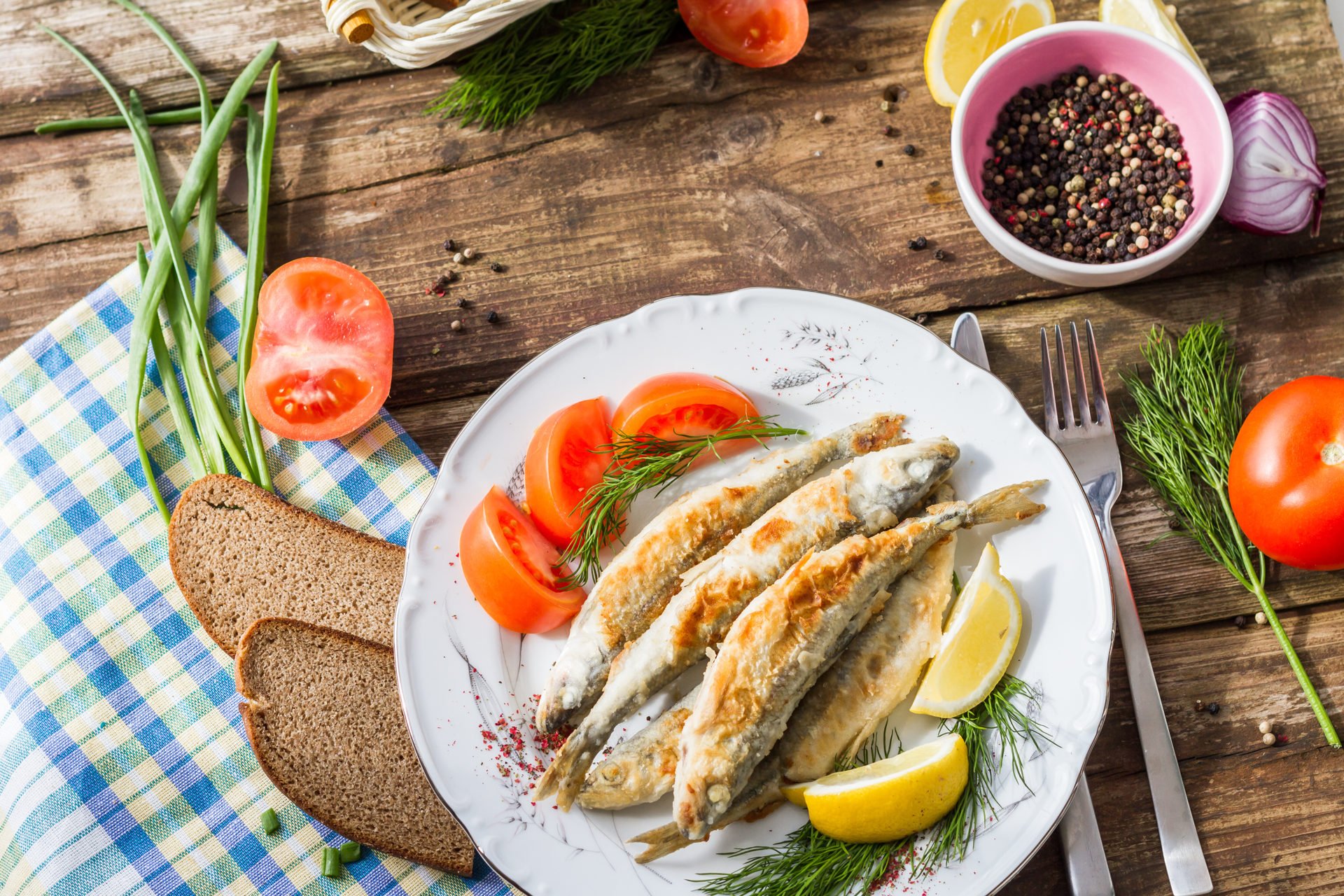 Fried fish smelt on a plate, served with lemon, tomatoes, onions and herbs
