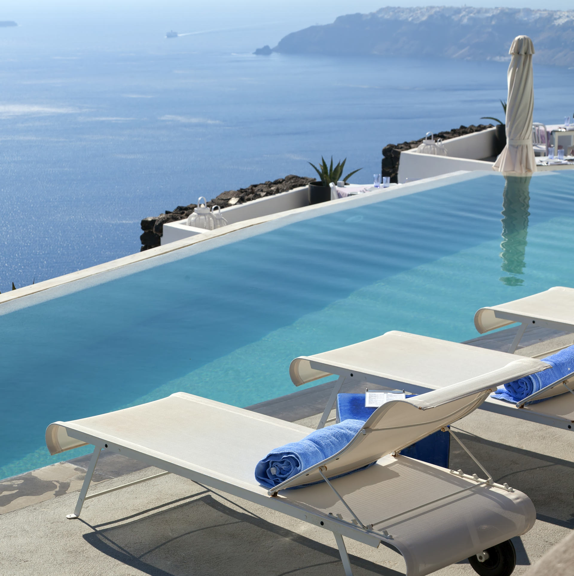 A luxury swimming pool situated in the town of Imerovigli on the Greek island of Santorini with a view of Oia in the distance.
