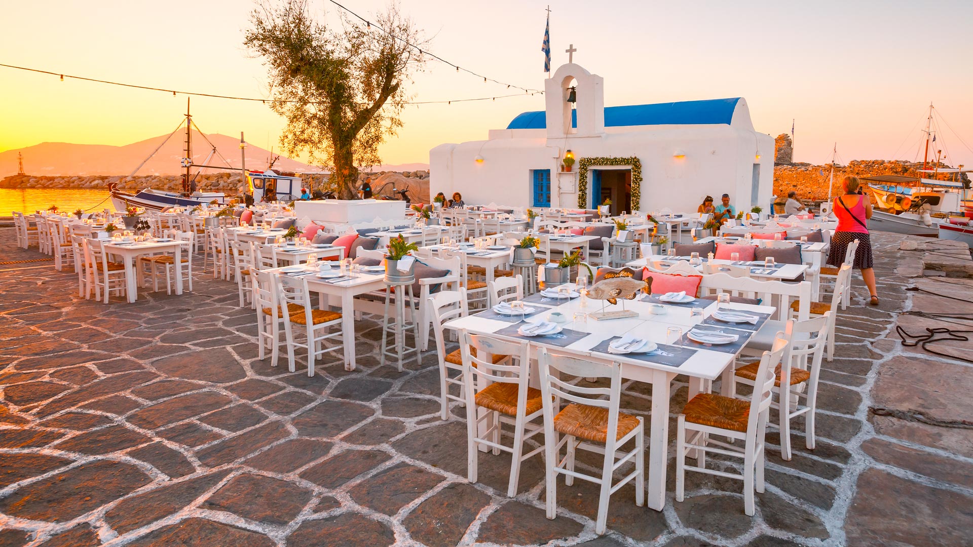 Tables of a restaurant in front of a church in the harbour of Naousa village, Paros island