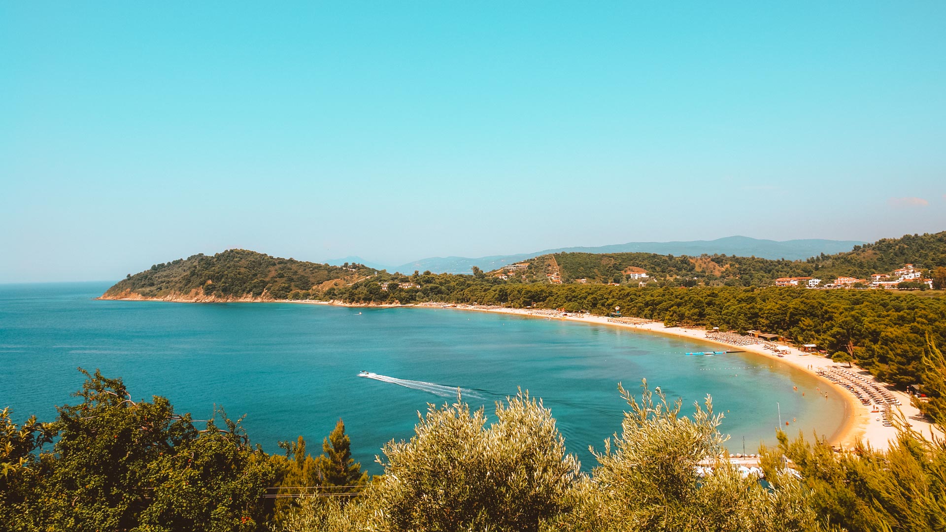 Its name comes from the Stone Pine trees that dominate the area and form a natural barrier with Lake Strofylia behind it