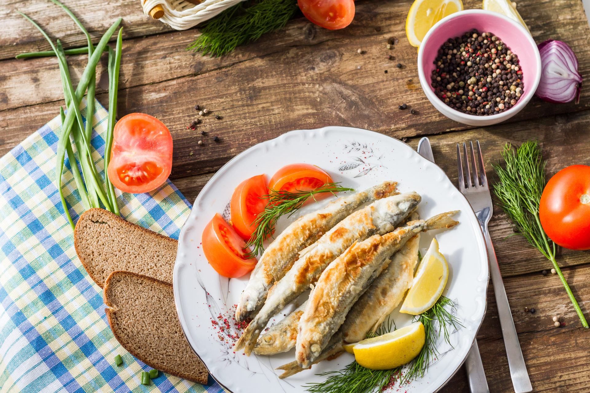 Fried fish smelt on a plate, served with lemon, tomatoes, onions and herbs