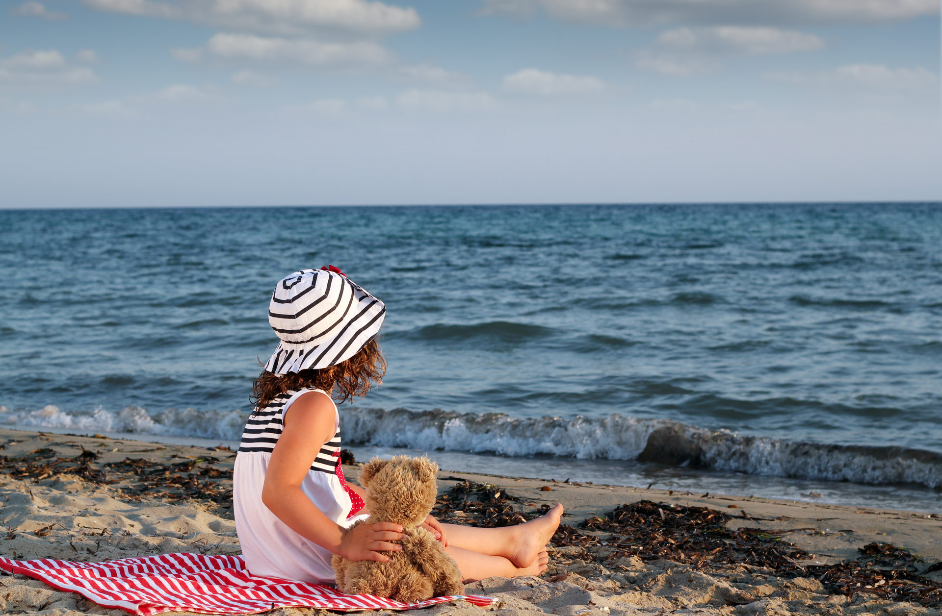 Little girl with teddy bear sitting on beach