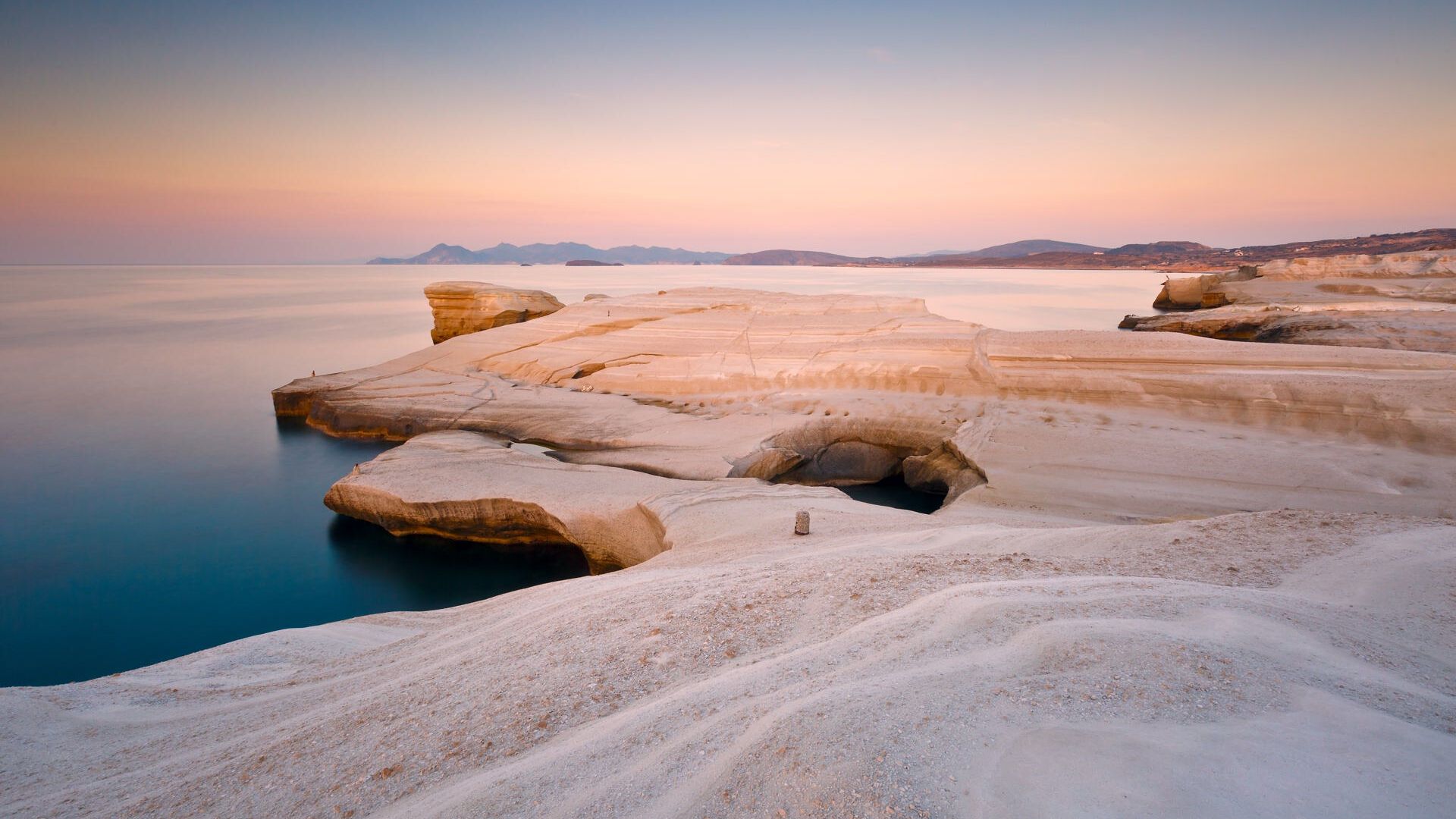 Coastal scenery with pale volcanic rocks near Sarakiniko beach in Milos island, Greece. Kimolos island can be seen in the distance.