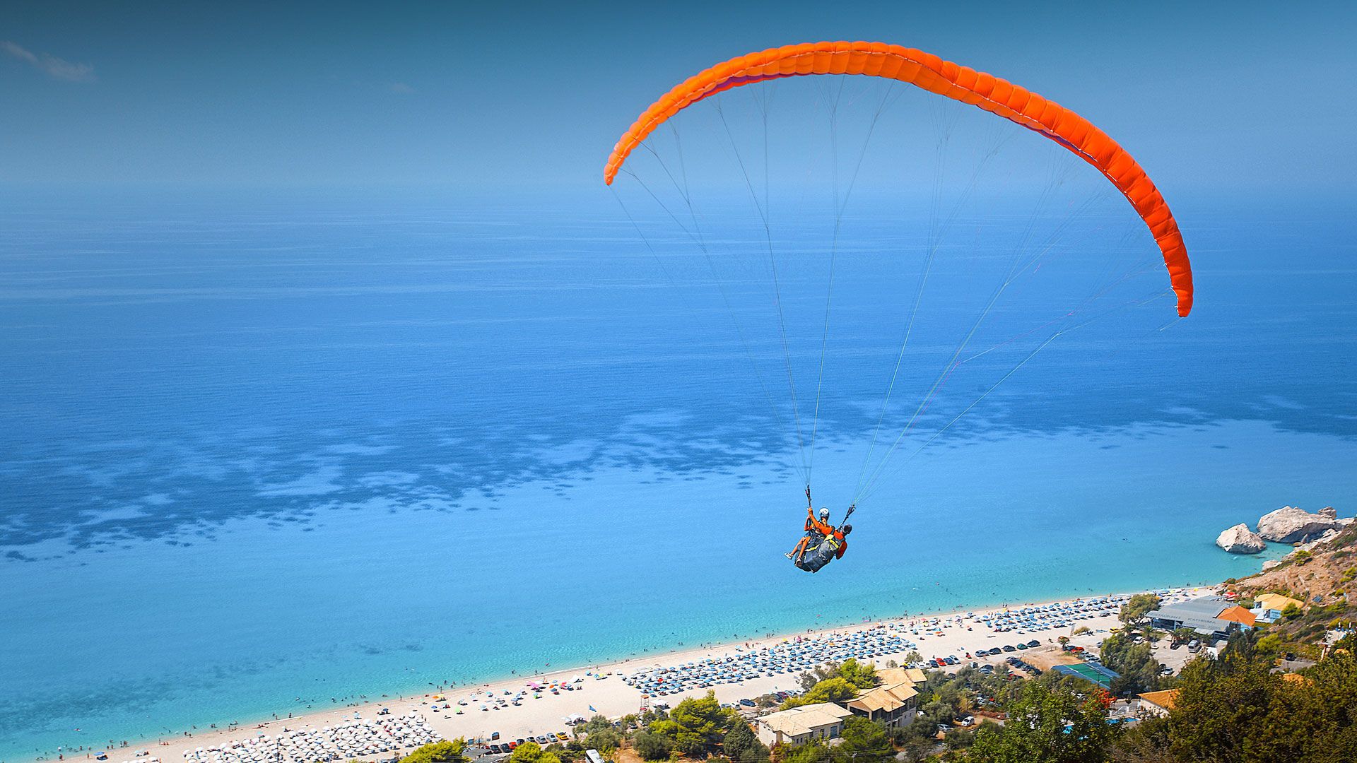 The sight of the paragliders, who launch from the green mountain backdrop and arc overhead before settling on the beach