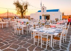 Tables of a restaurant in front of a church in the harbour of Naousa village, Paros island