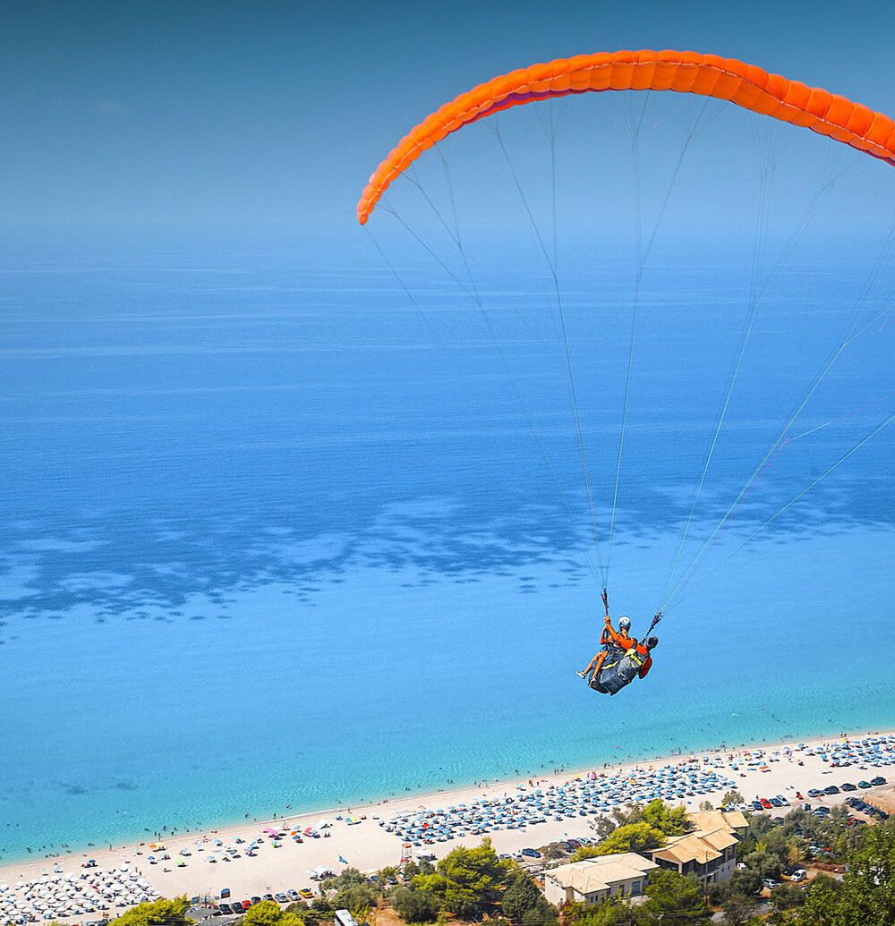 The sight of the paragliders, who launch from the green mountain backdrop and arc overhead before settling on the beach