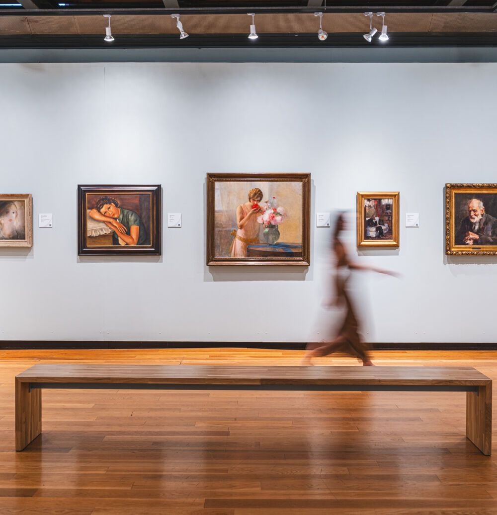 Interior of the Municipal Gallery of Chania, one of the Chania museums, with paintings displayed on a white wall and a wooden bench in the foreground