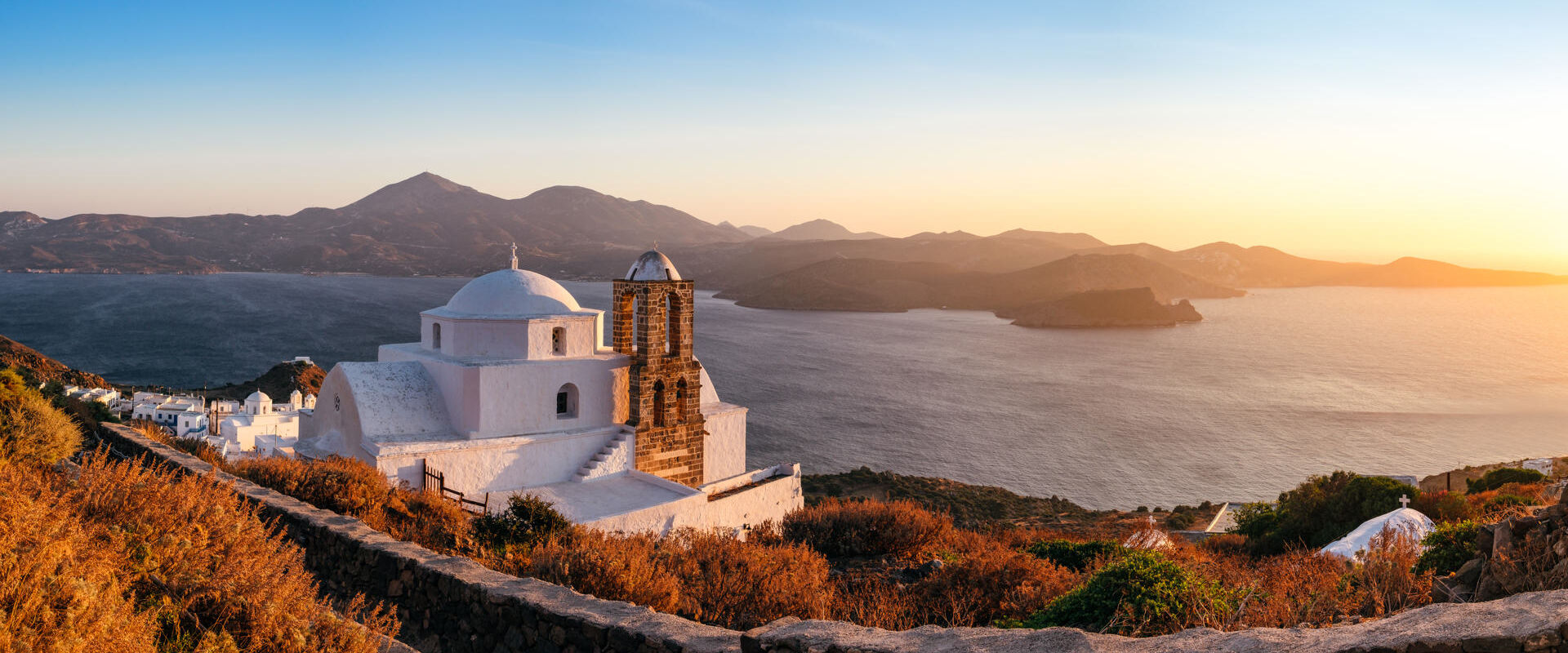 Panoramic view of traditional Greek church, village and ocean coast, Plaka village on Milos island, Greece