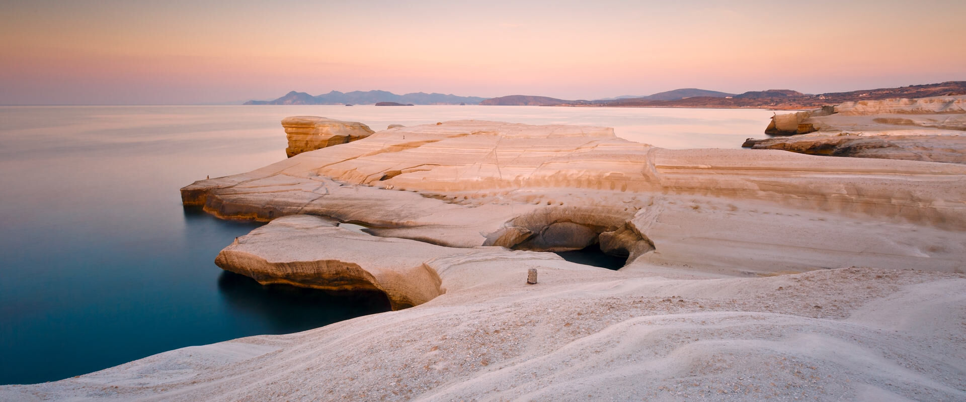 Coastal scenery with pale volcanic rocks near Sarakiniko beach in Milos island, Greece. Kimolos island can be seen in the distance.