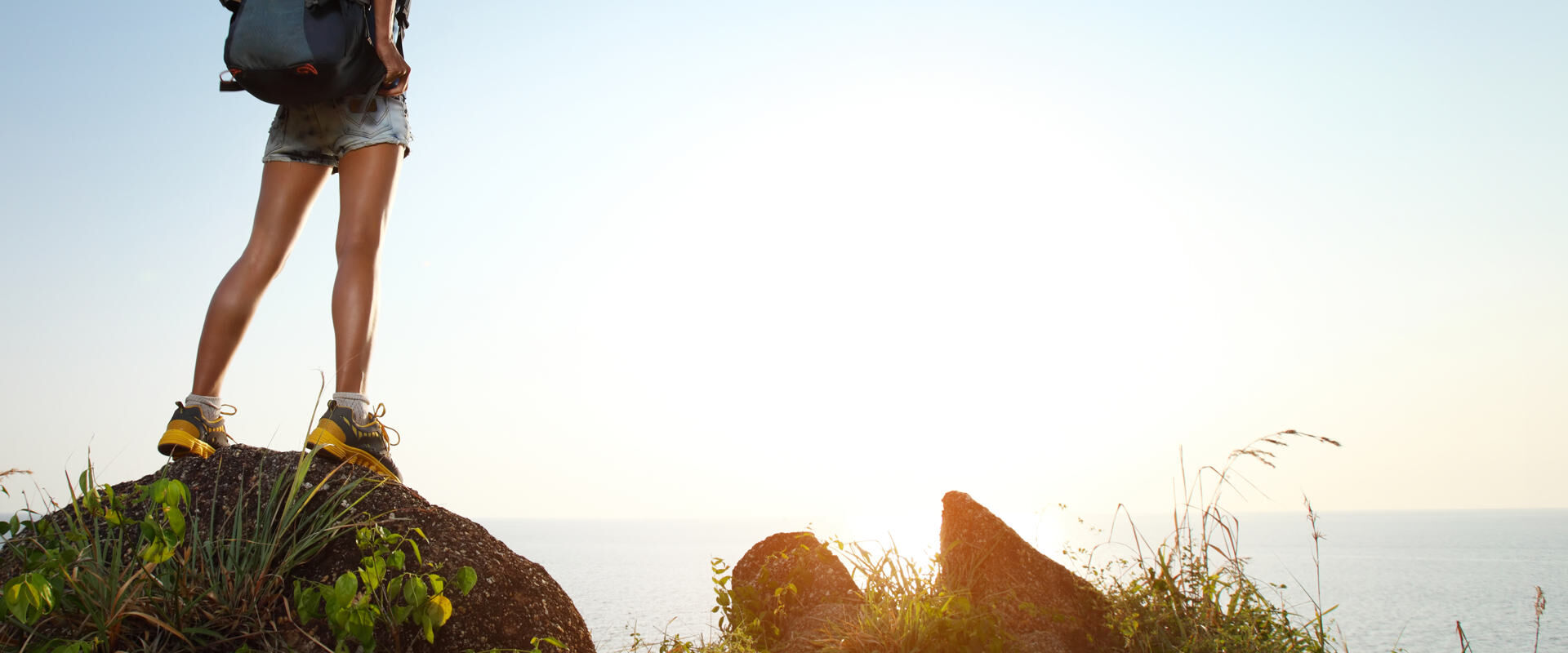 Junger Tourist mit dem Rucksack, der auf einem Felsen steht und Sonnenuntergang genießt