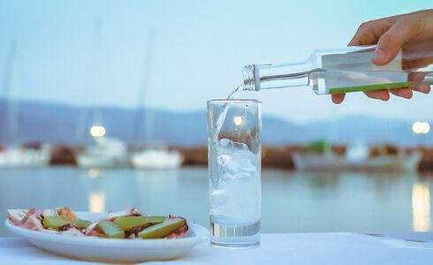 A crystal clear liquid is poured into a glass and in drops an ice cube, instantly emitting magical swirls of white
