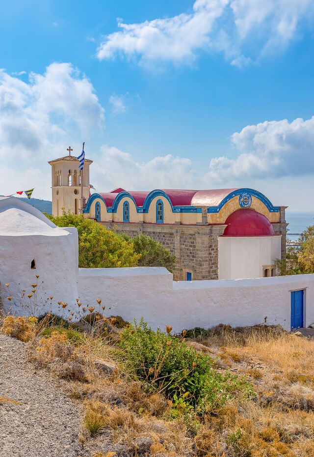 Traditional church with red domes and a bell tower in Kasos, set against a bright blue sky.