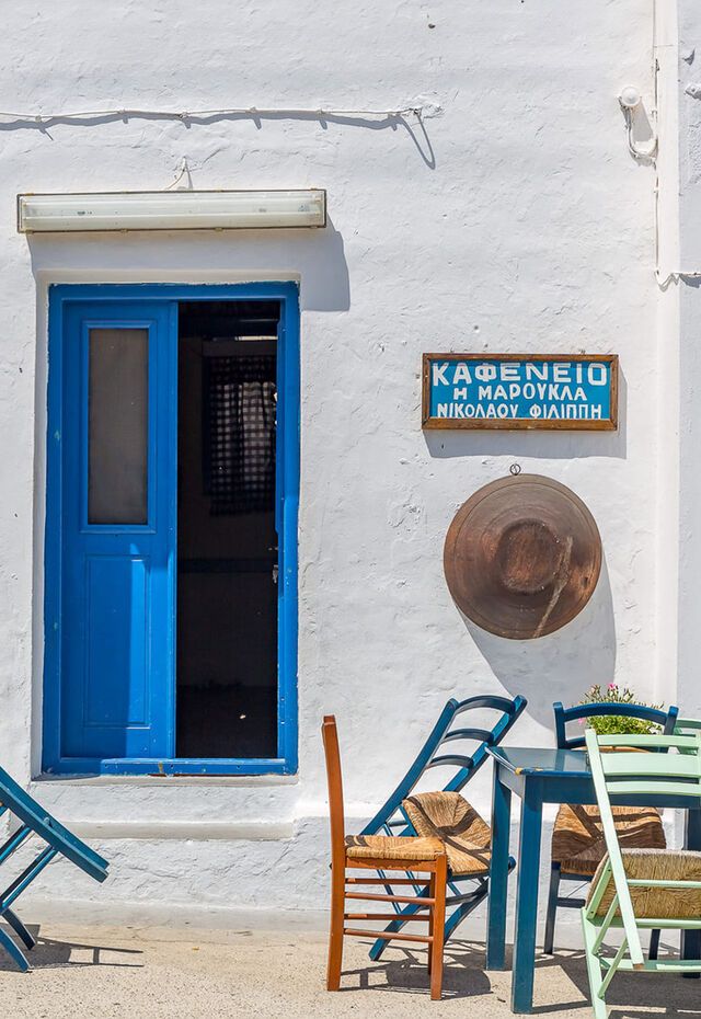 Traditional kafeneio in Kasos with a blue door, white walls, and colorful chairs outside.