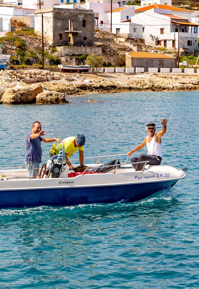 Three men on a boat waving near the coast of Fri in Kasos