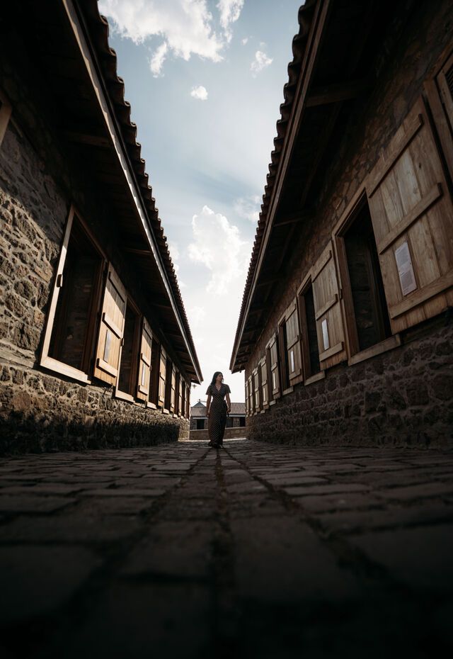 Narrow cobbled passage between stone museum buildings at the Museum of Industrial Olive-Oil Production of Lesvos, with a visitor walking through.