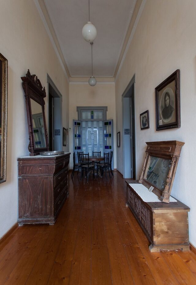 A long hallway inside the Folklore Museum at Vatousa with wooden floors, antique furniture and framed portraits.