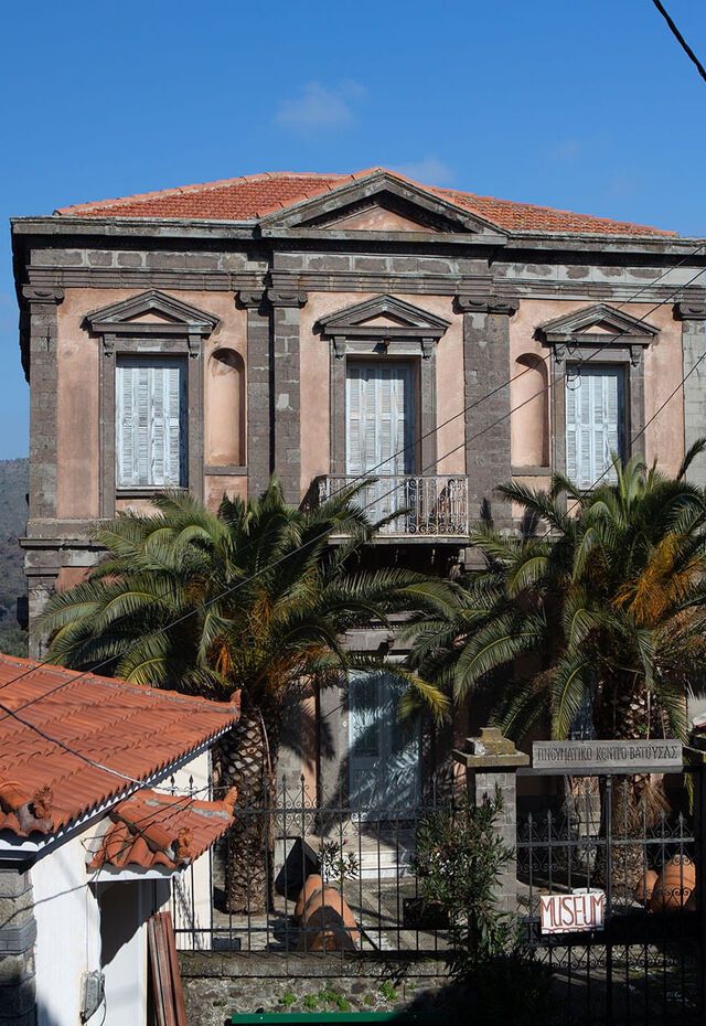 The Folklore Museum at Vatousa building seen from outside, with palm trees in front and hills in the background.