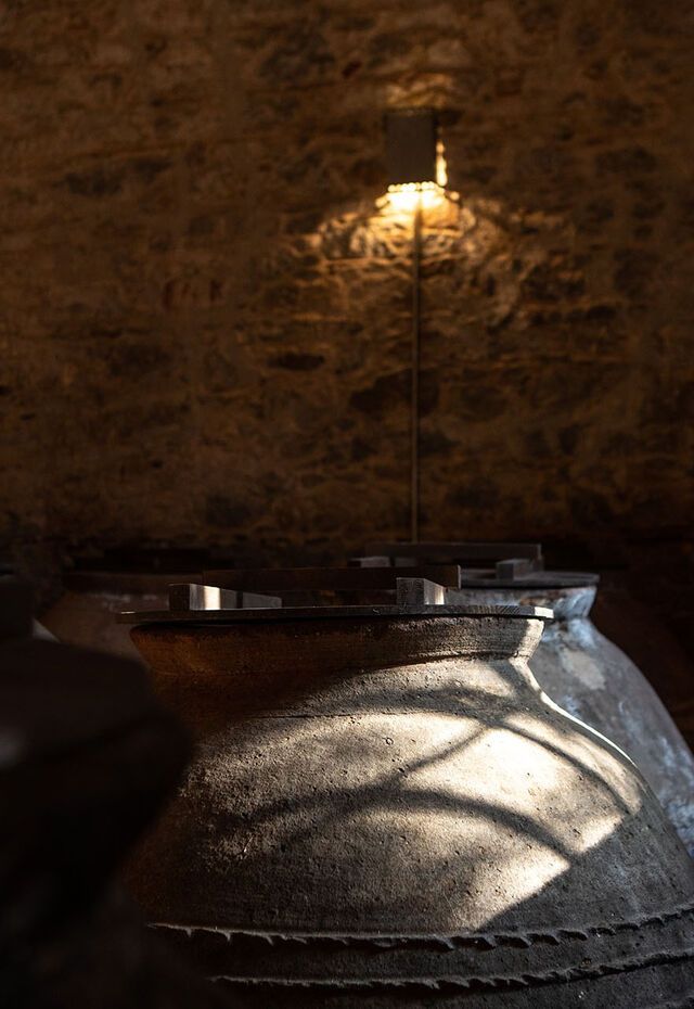 Traditional clay storage jars inside a dim, stone-walled room at The Vranas Olive Press and Museum, lit by warm wall lights.