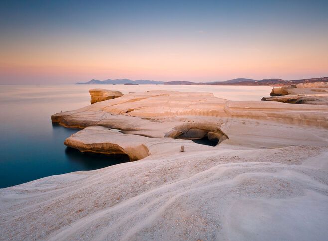 Coastal scenery with pale volcanic rocks near Sarakiniko beach in Milos island, Greece. Kimolos island can be seen in the distance.