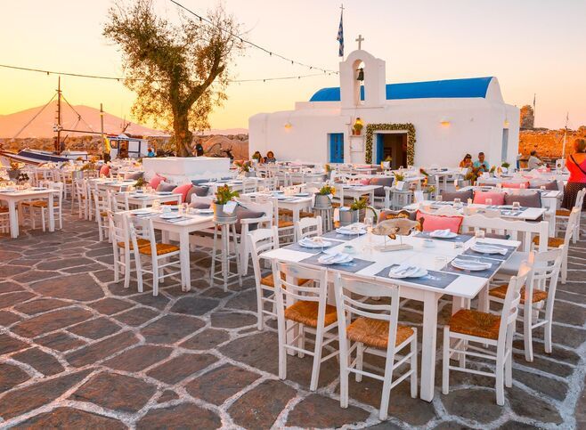 Tables of a restaurant in front of a church in the harbour of Naousa village, Paros island