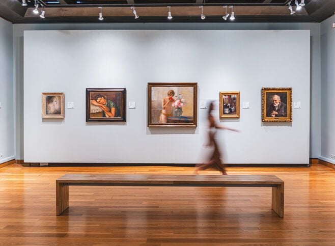 Interior of the Municipal Gallery of Chania, one of the Chania museums, with paintings displayed on a white wall and a wooden bench in the foreground