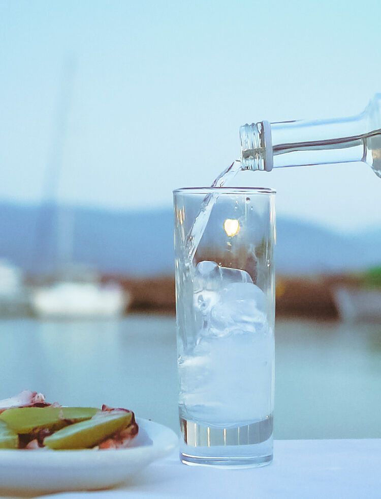 A crystal clear liquid is poured into a glass and in drops an ice cube, instantly emitting magical swirls of white