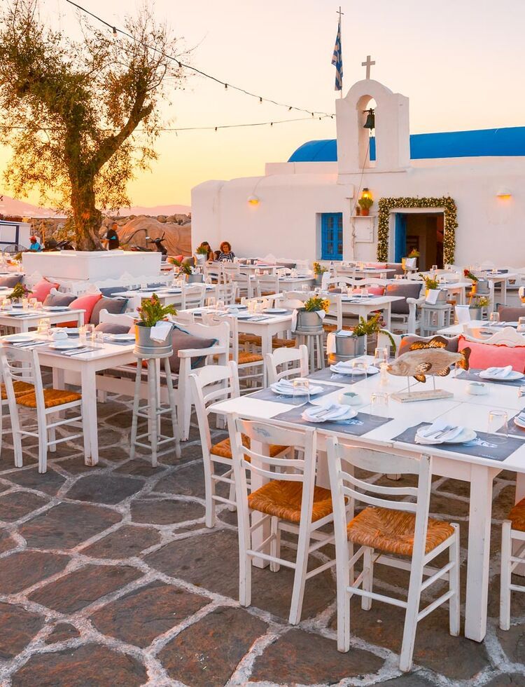 Tables of a restaurant in front of a church in the harbour of Naousa village, Paros island